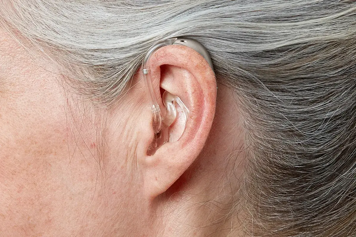 Orelha de uma mulher de cabelos grisalhos usando aparelho atrás da orelha, com um tubo fino e transparente