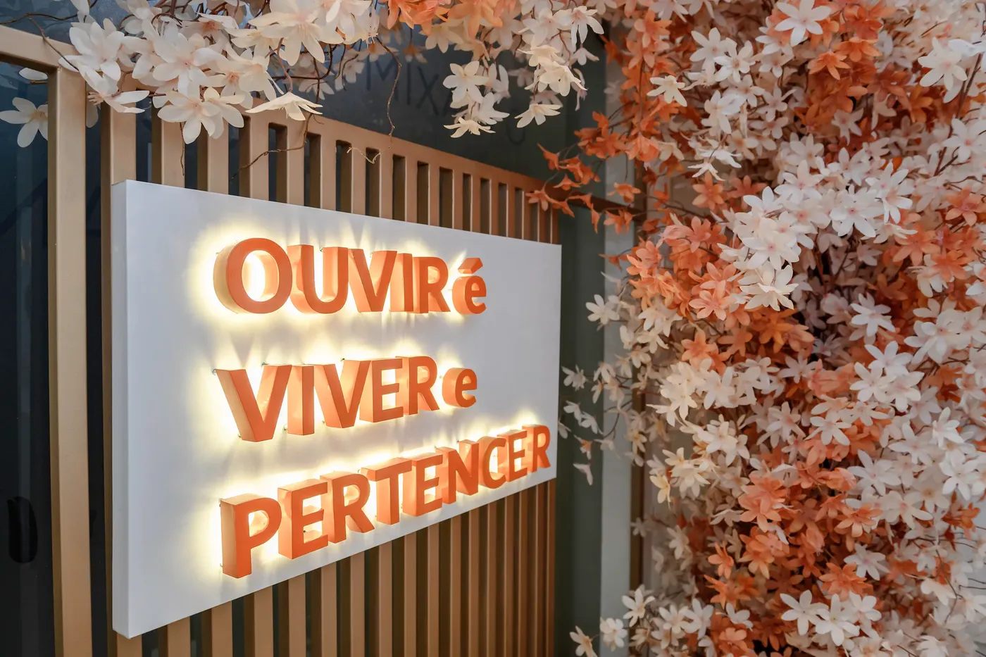 Letreiro iluminado da clínica com a frase Ouvir é viver e pertencer, entre flores