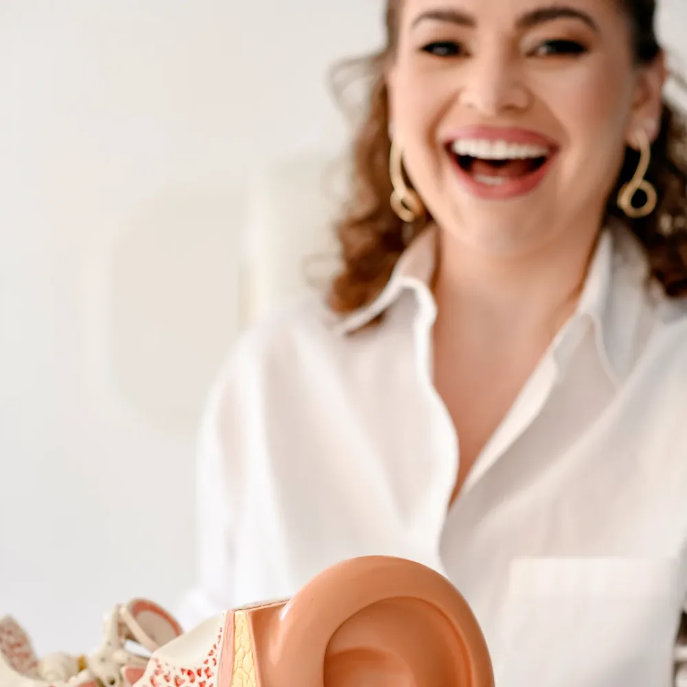 Fonoaudióloga da Hear Clean sorrindo, ao lado de um modelo anatômico do ouvido