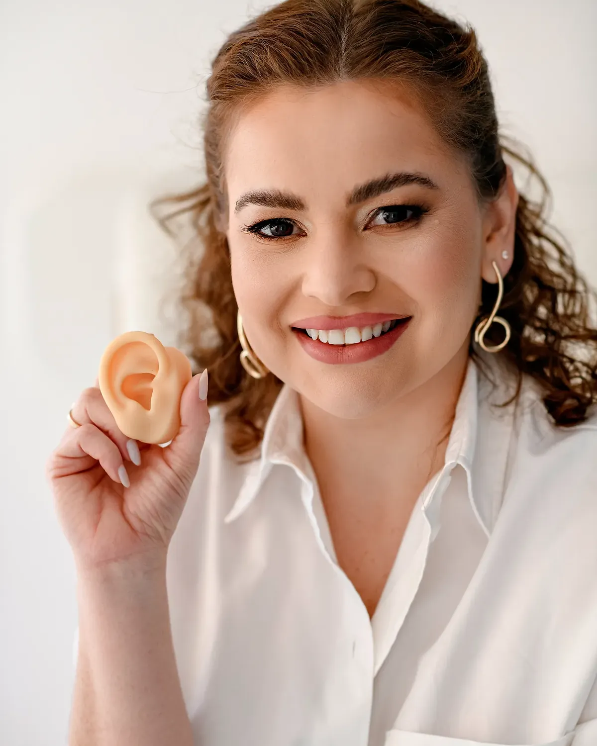 Fonoaudióloga da Hear Clean sorrindo, segurando um modelo de orelha em silicone